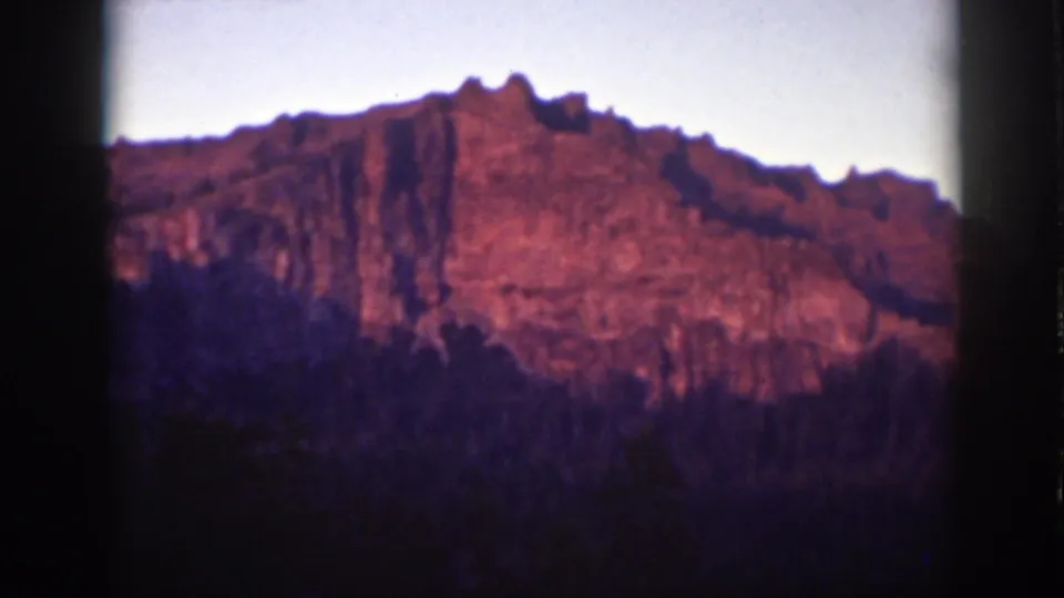 1939 Lake Tahoe 8mm frame of a warm-toned mountainside set against pale sky and deep forest shadow.