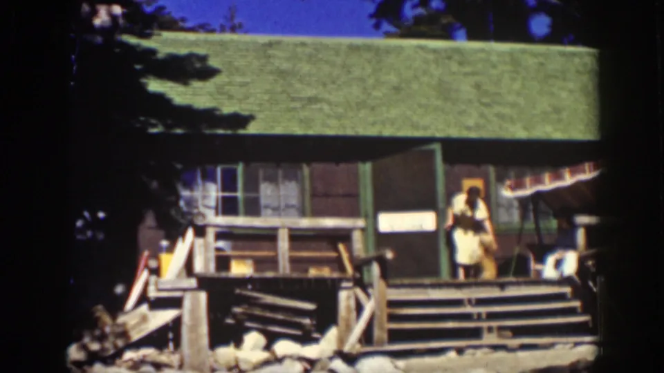 1939 Lake Tahoe cabin exterior with a person on the porch appearing to interact with a small dog near the doorway.
