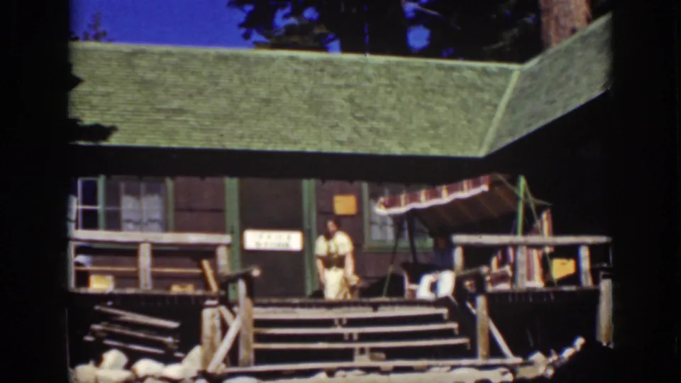 Late-1930s Lake Tahoe home-movie frame showing a woman and dog on a rustic cottage porch.