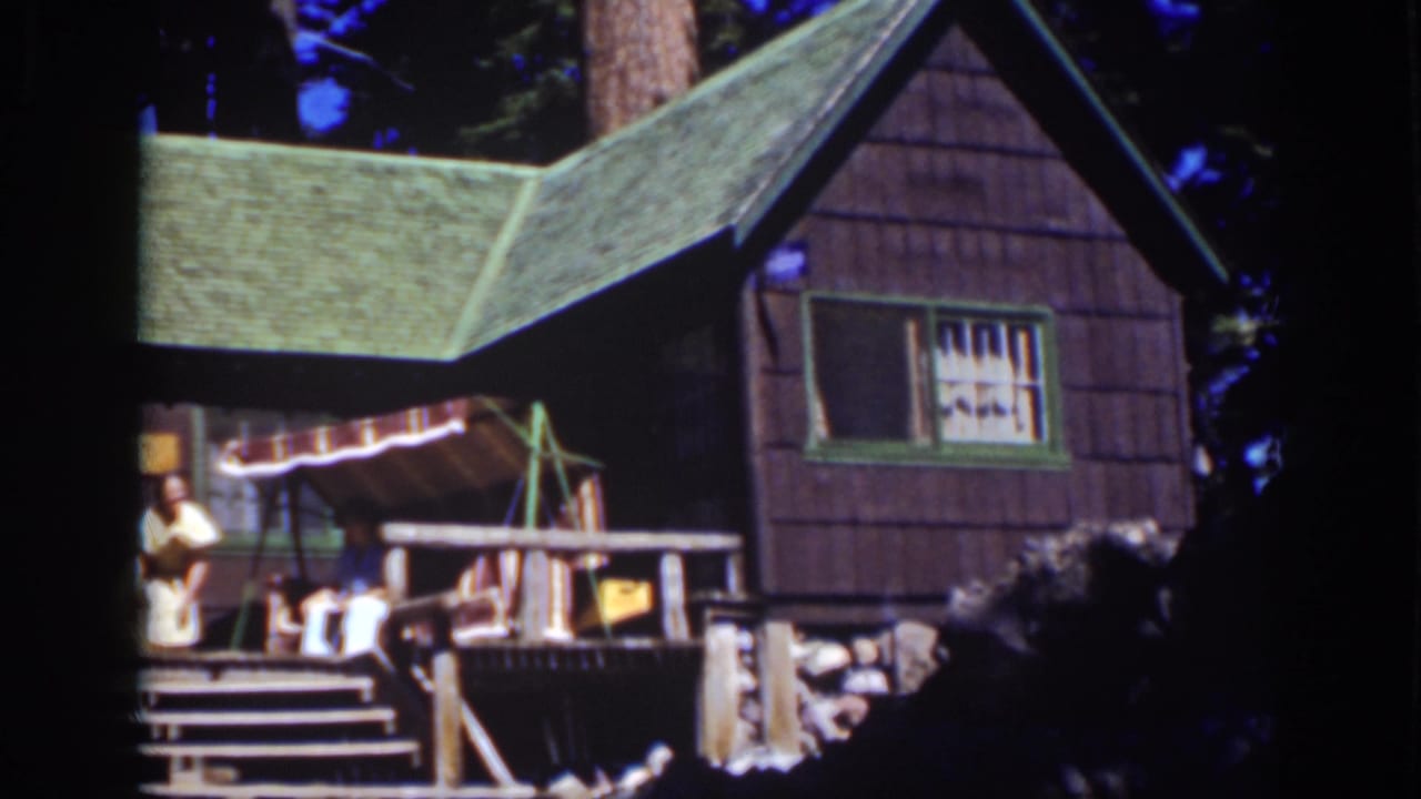 Rustic cabin porch with a woman at left, a seated person, striped awning, and green roof.
