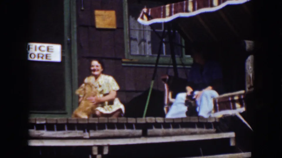 At a Lake Tahoe cabin porch in 1939, a smiling woman sits with a golden dog while another adult rests in a striped porch swing.