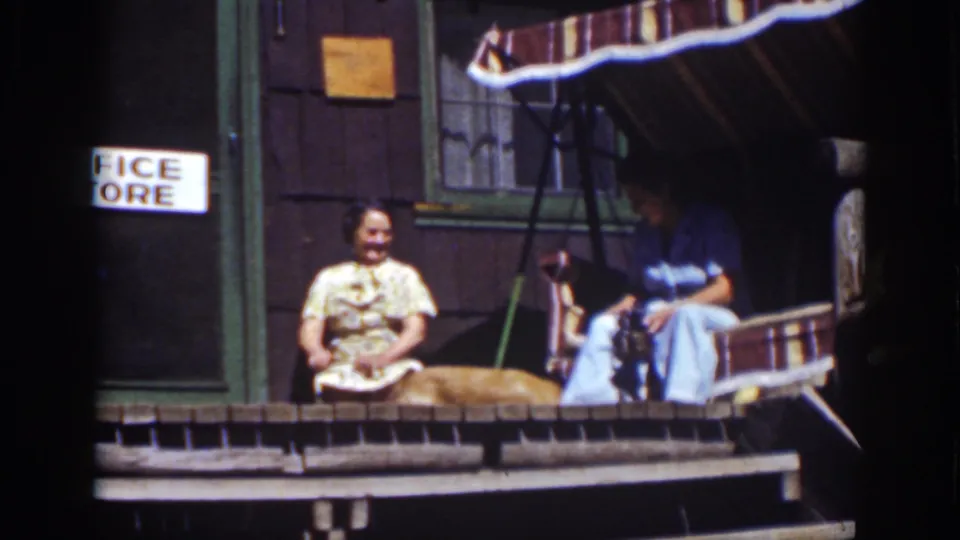 The dog lies across the 1939 Lake Tahoe cabin porch as the woman sits nearby and another adult remains in the striped swing.