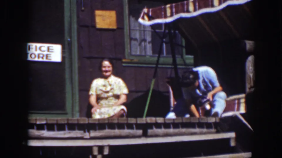 1939 Lake Tahoe home-movie frame with the man leaning down, possibly adjusting a shoe, beside a woman on a cabin porch.