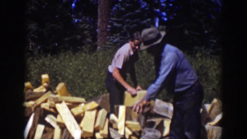 Lake Tahoe 1939 home-movie still showing an older man and younger companion bent over a woodpile during firewood splitting.