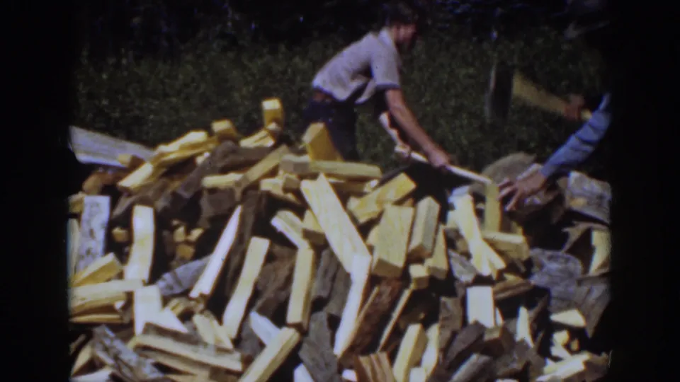 In 1939 Lake Tahoe home-movie footage, a man works with an axe near a large split firewood pile while another adult is partly visible.