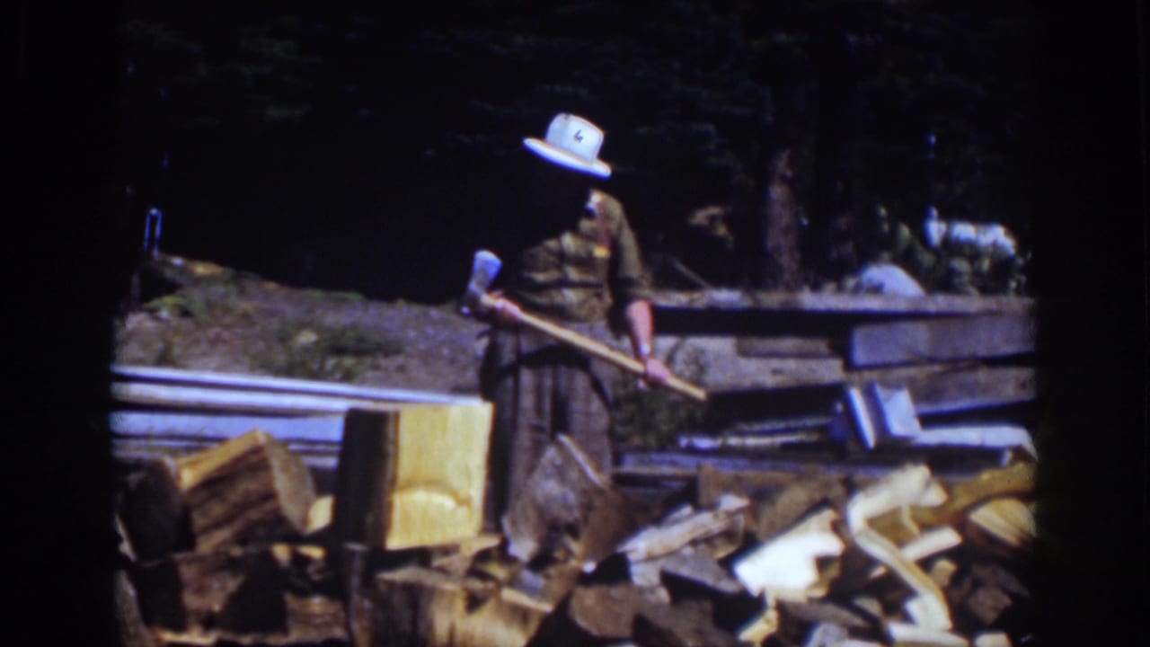 At Lake Tahoe in 1939, a man in a white hat stands with an axe beside a chopping block and scattered firewood in a forested outdoor area.