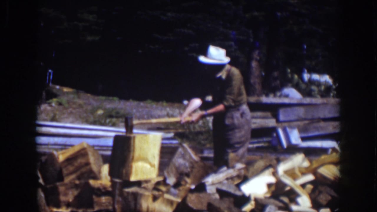 At Lake Tahoe in 1939, the man leans over a chopping block with an axe, surrounded by split logs and a wooded background.