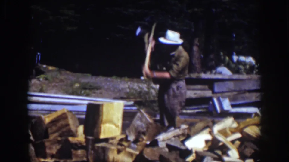 At Lake Tahoe in 1939, the man raises an axe to split wood, with a chopping block, scattered logs, and trees visible around him.