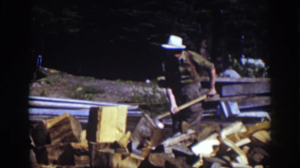 At Lake Tahoe in 1939, the man follows through with the axe near a chopping block amid split firewood and a shaded forest backdrop.