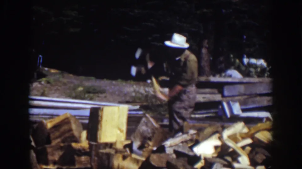 The man in the white hat bends over the chopping block with an axe, surrounded by split wood in the 1939 Lake Tahoe outdoor scene.