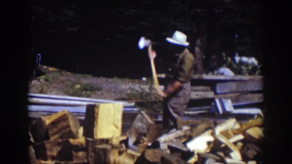 A man pauses with the axe beside the chopping block, with rough lumber and firewood visible in the 1939 Lake Tahoe home-movie frame.