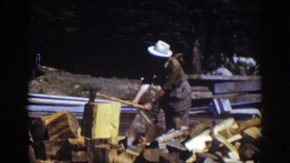 The man leans into another chop near the block, with piles of split firewood and shaded trees behind him in the Lake Tahoe footage.