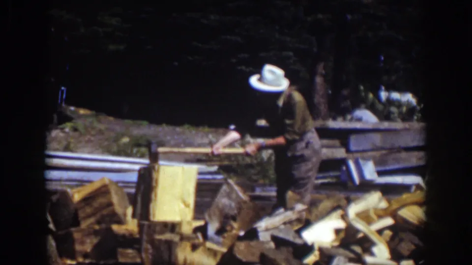 The home-movie frame shows the man leaning toward the chopping block amid firewood in a sunny Lake Tahoe outdoor setting.