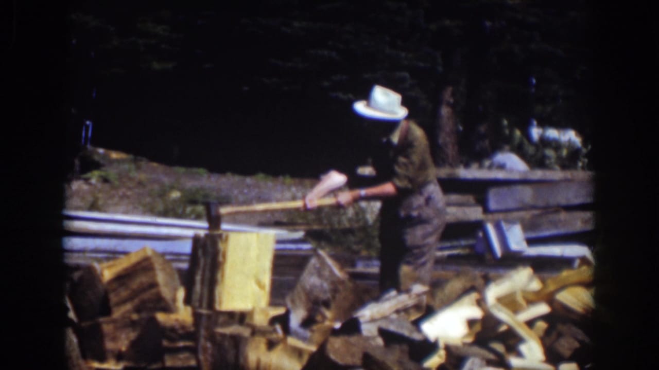 At Lake Tahoe in 1939, a man in a white hat swings an axe near stacked logs and rough lumber in a wooded outdoor area.