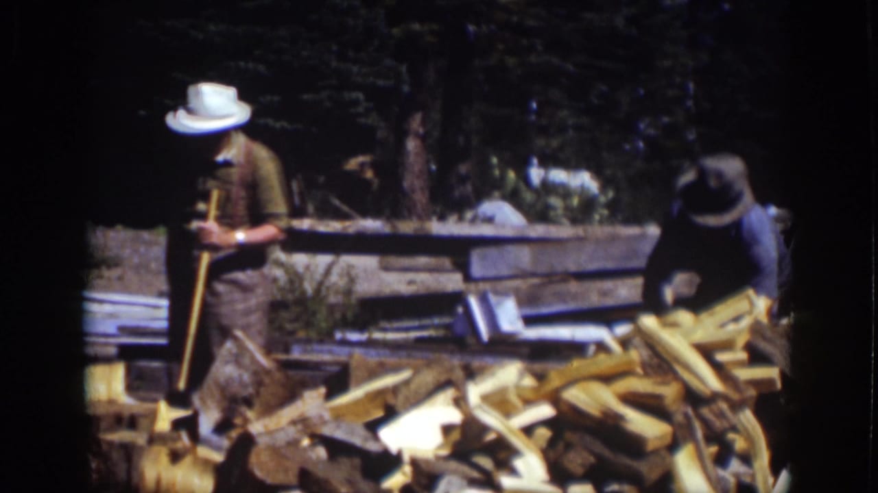 Two men at Lake Tahoe in 1939 work around a pile of cut wood, with one holding an axe and the other bending near the lumber.