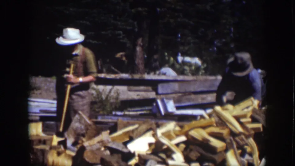 Two men at Lake Tahoe in 1939 work around a pile of cut wood, with one holding an axe and the other bending near the lumber.