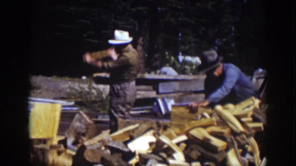 A man in a white hat swings an axe as another man in a dark hat works beside stacked lumber and chopped wood in the 1939 Lake Tahoe footage.