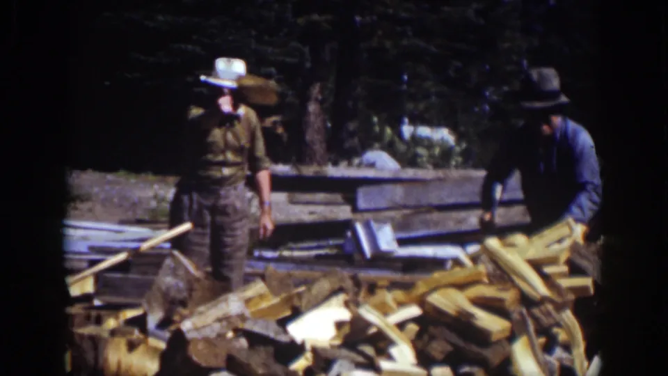 In the Lake Tahoe home-movie scene, one man in a white hat stands while another works beside a pile of split wood.