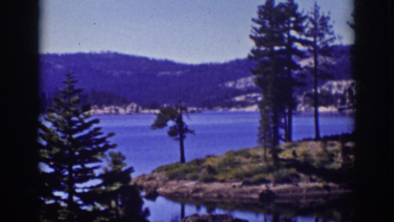 Pine-covered shoreline beside a blue lake with distant hills and dark film borders.