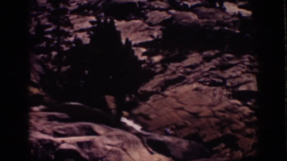 1939 Lake Tahoe home-movie frame showing pine silhouettes, pale boulders, and rough rock slopes in warm, grainy 8mm color.