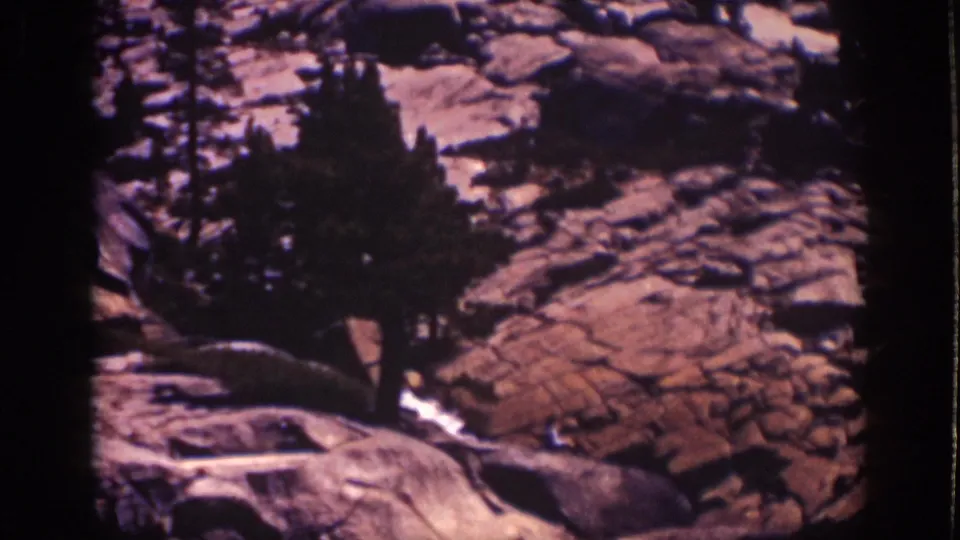 Lake Tahoe, California frame with dark conifers, pale rock forms, and possible water highlights in a grainy 1939 8mm view.