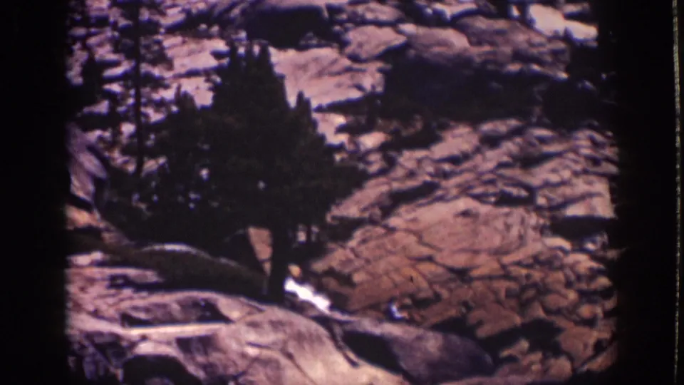 Late-1930s Lake Tahoe landscape frame with pine silhouettes, uneven rock surfaces, and warm color shift from scanned 8mm film.