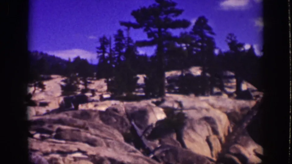 1939 Lake Tahoe 8mm frame showing pale granite boulders, pine silhouettes, and a saturated blue-purple sky.