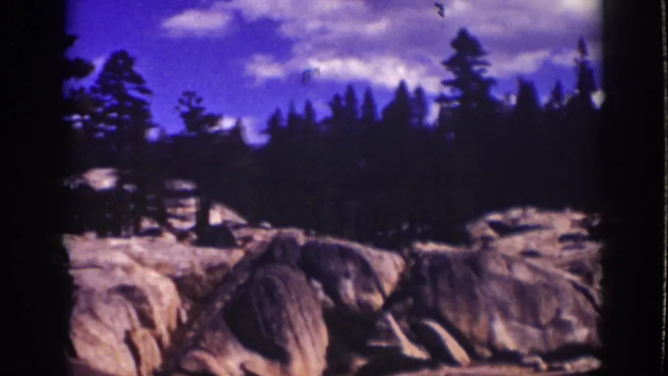 1939 Lake Tahoe landscape frame showing a darker pine line and pale boulders as the handheld pan moves right.