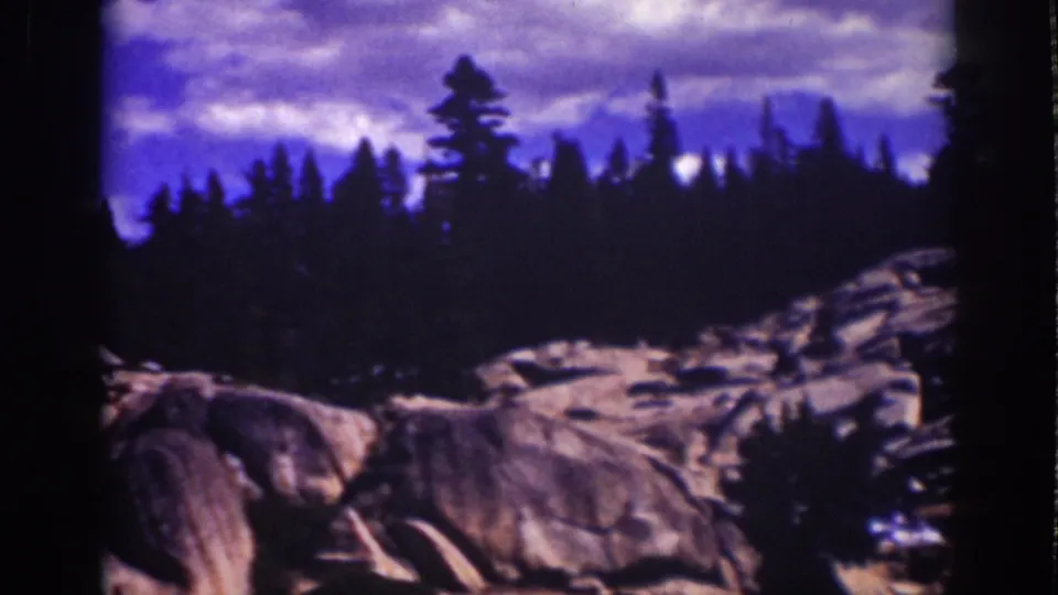 Final Lake Tahoe frame with a rocky slope, shadowed pines, and cloud streaks in a blue-purple sky.