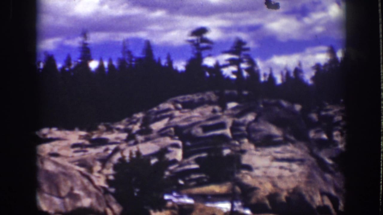 Granite cliff face and silhouetted evergreens beneath a clouded sky.