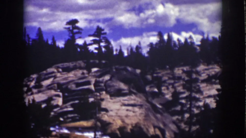 1939 Lake Tahoe home-movie view across granite terrain, conifers, and distant light mountain forms under a mottled sky.