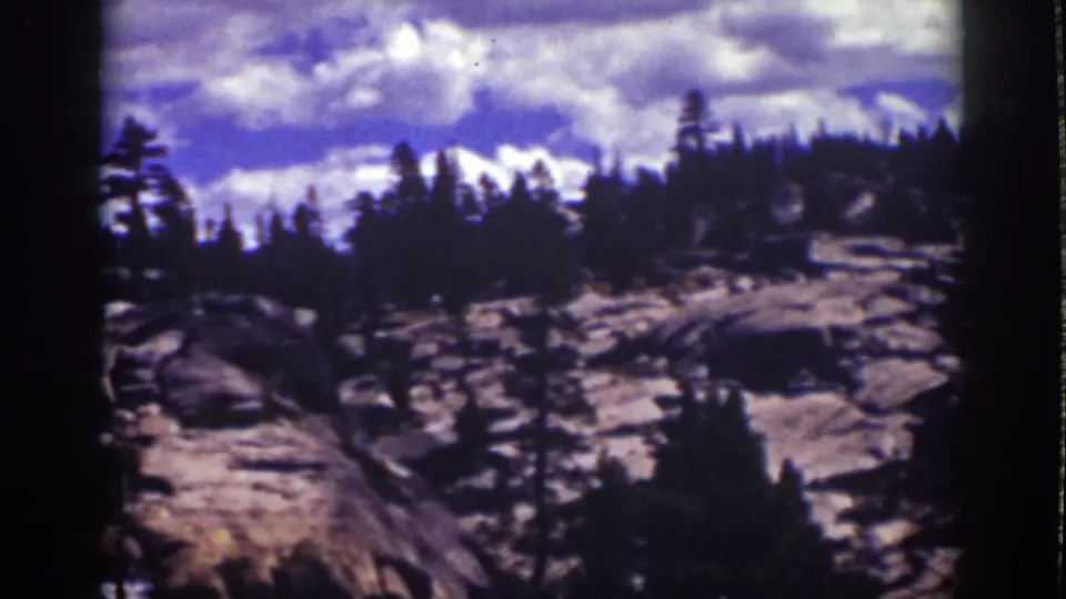 Late pan frame from 1939 Lake Tahoe showing a rocky watercourse or dry stream bed, conifers, and clouded sky.