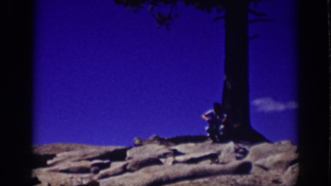 1939 Lake Tahoe frame with a man sitting close to a tree trunk for shade on a rocky slope.