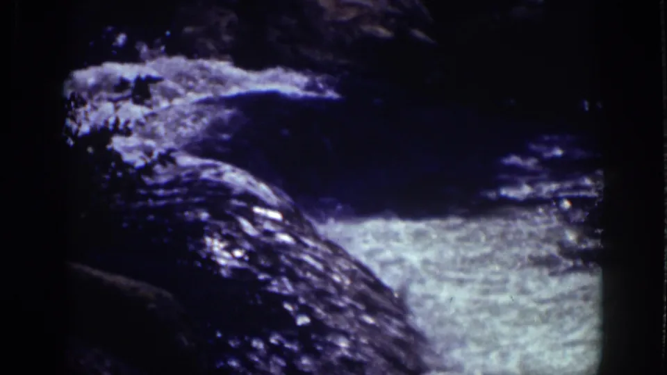 Close 1939 Lake Tahoe home-movie view of fast-moving water churning over rocks, rendered with dark shadows and blue cast.