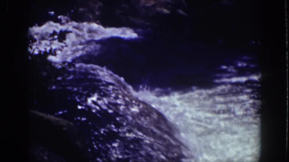 1939 Lake Tahoe 8mm frame showing fast water cascading across dark rocks with bright foam and blue-purple shadow.