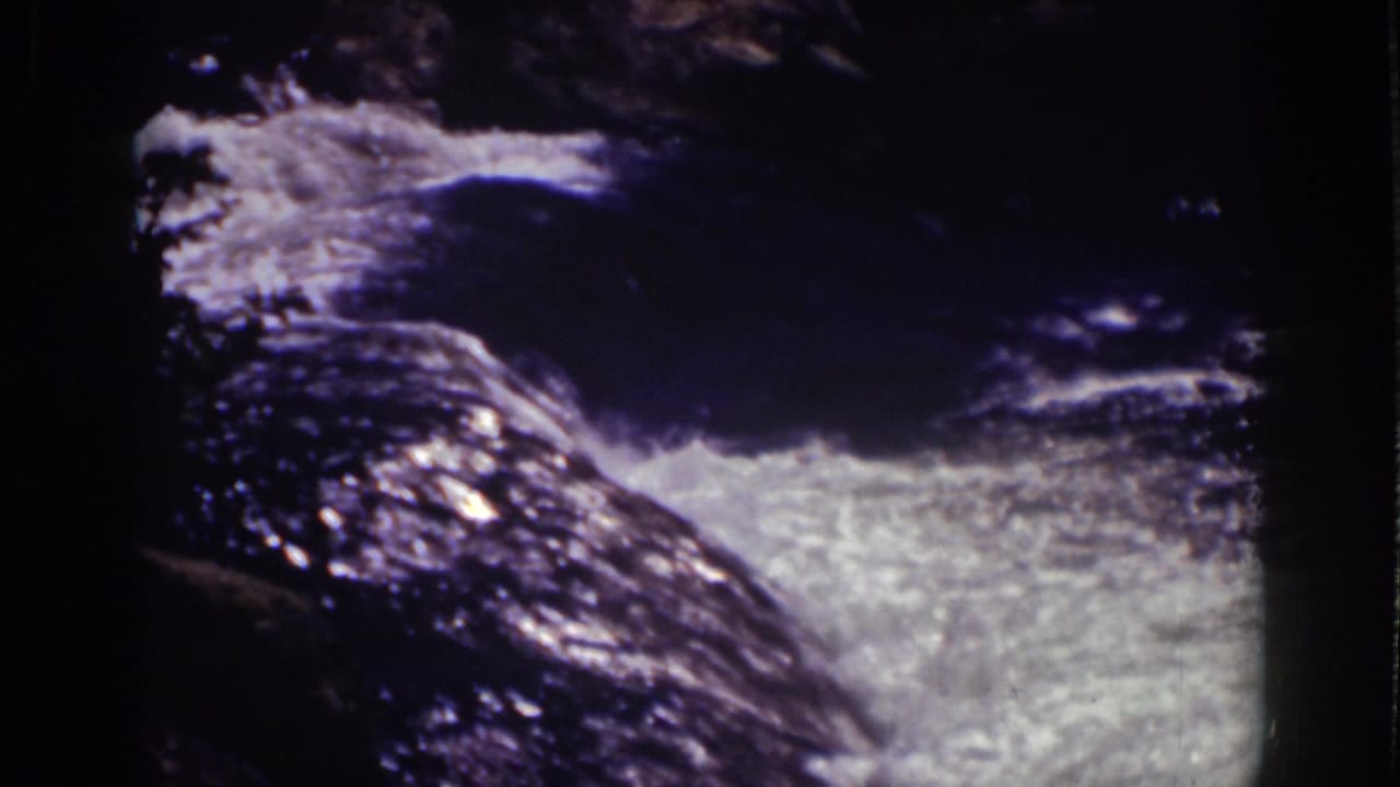 Whitewater rushing over dark rocks in a shadowed mountain stream.