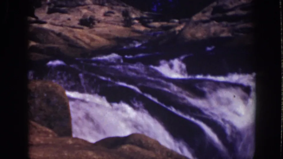 1939 Lake Tahoe 8mm frame with turbulent white water passing over dark rocks in a forested setting.