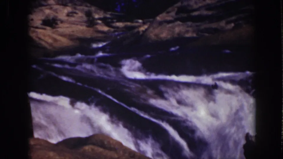 1939 Lake Tahoe frame showing foamy water rushing past dark rock forms in aged color 8mm footage.