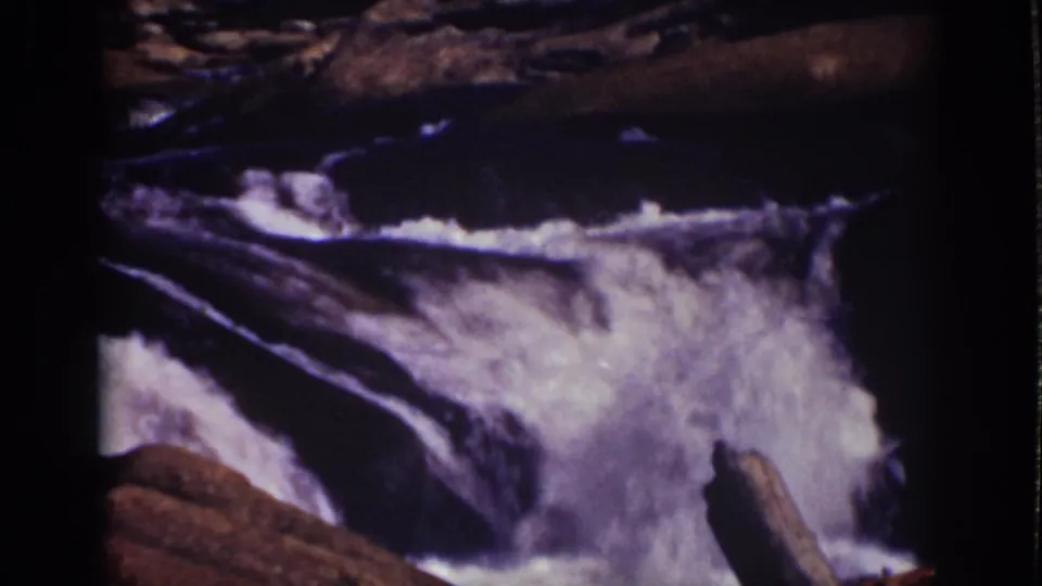 1939 Lake Tahoe 8mm frame with foaming water spilling over a rocky ledge in a mountain stream.