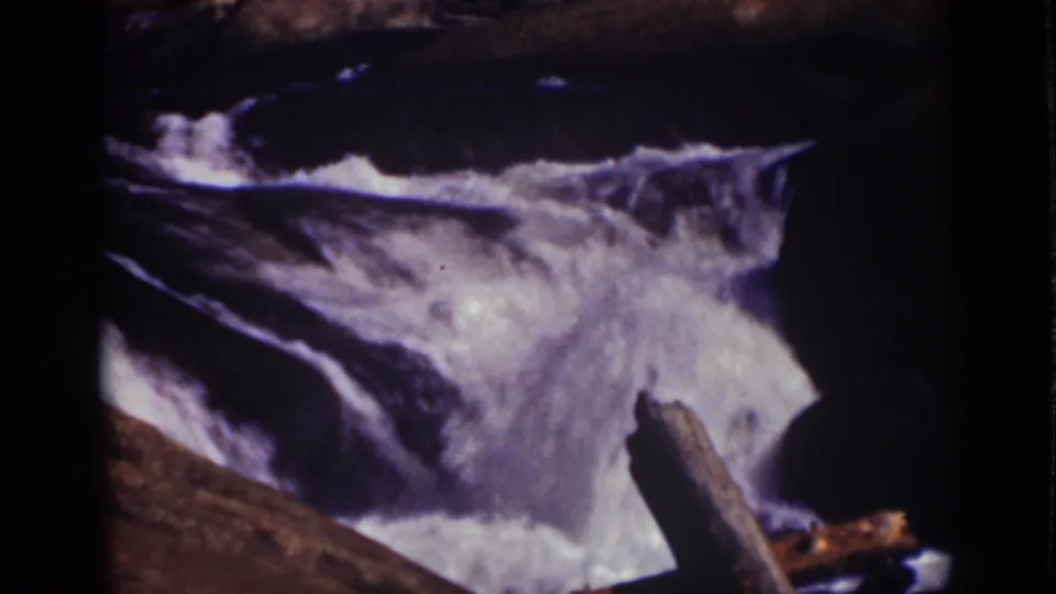 1939 Lake Tahoe home-movie frame showing turbulent stream water, rocks, and a leaning branch near the cascade.