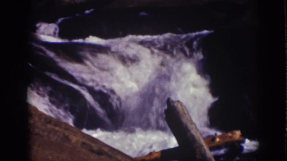 1939 Lake Tahoe 8mm frame of bright white water churning around rocks, with a branch near the foreground.