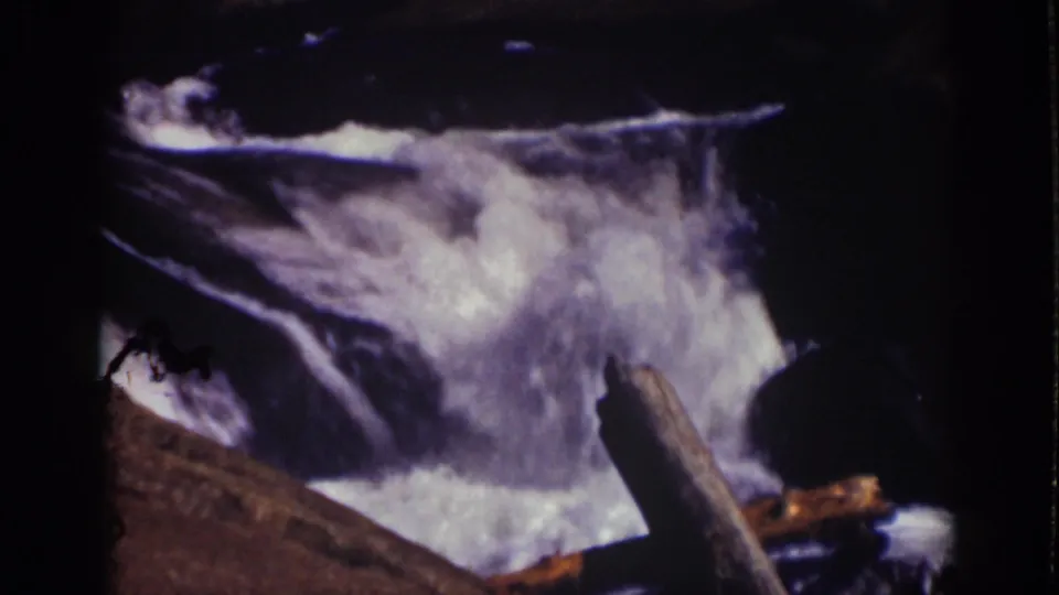 1939 Lake Tahoe home-movie frame showing frothy stream water cascading past dark rocks and a foreground log.
