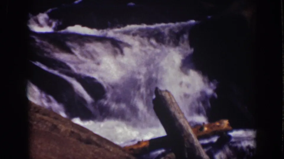 Lake Tahoe 8mm frame of bright foamy water moving over dark rocks, with a weathered log in front.