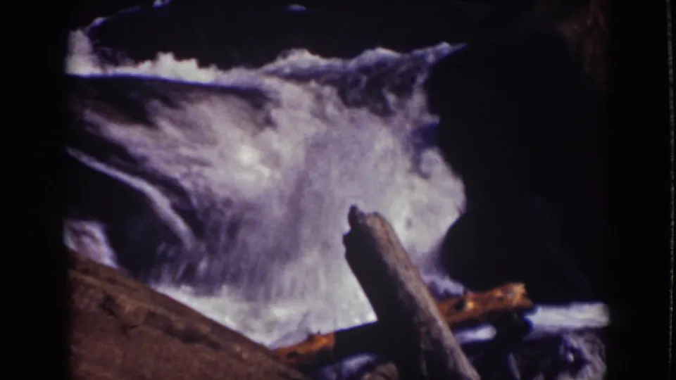 Lake Tahoe home-movie still showing a bright whitewater cascade, dark rock edges, and a foreground log.