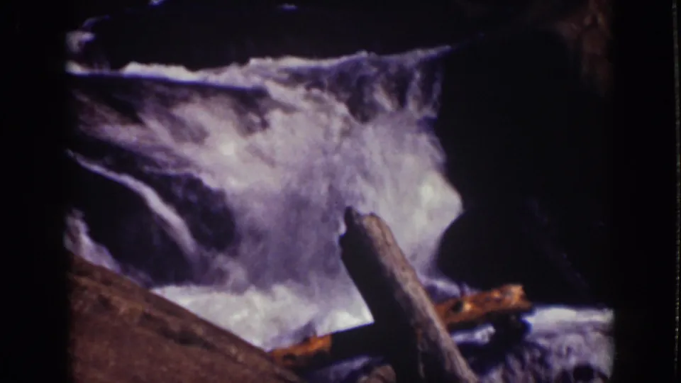 Close 8mm view of a foaming waterfall in the Lake Tahoe region, with logs and dark rock edges in frame.
