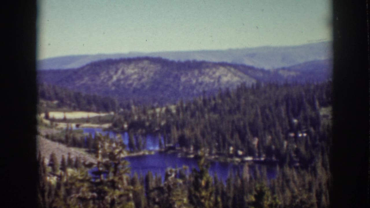 Blue lake among pine forest and rolling hills viewed from above.