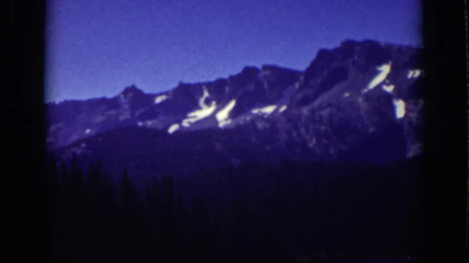 Twilight-toned Lake Tahoe-area mountain view with dark forest, jagged peaks, and snow patches on the ridgeline.