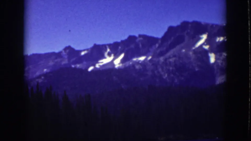 1939 Lake Tahoe home-movie frame showing distant snow-streaked mountains beyond a dark evergreen tree line.