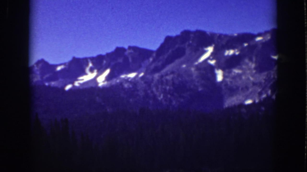 Lake Tahoe-area 8mm frame from 1939 with rugged peaks, bright snow patches, and dense evergreens below.