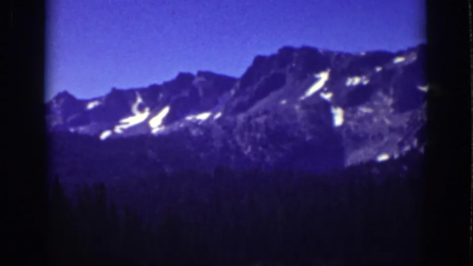 Lake Tahoe-area 8mm frame from 1939 with rugged peaks, bright snow patches, and dense evergreens below.
